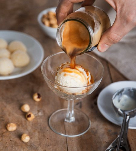 Pouring Lavazza Crema E Gusto K-Cup Pods coffee over ice cream on a wooden surface with hazelnuts and cookies